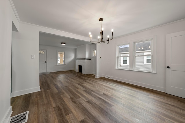 unfurnished living room featuring dark hardwood / wood-style flooring, crown molding, a fireplace, and a chandelier