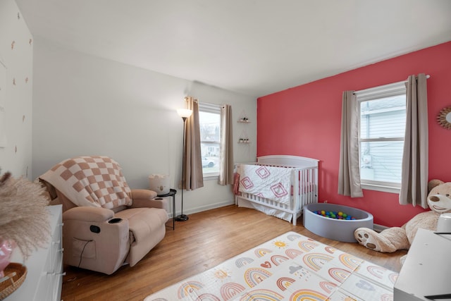 bedroom featuring multiple windows, hardwood / wood-style flooring, and a crib