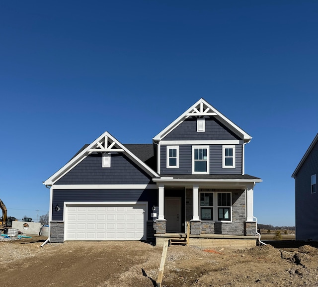 craftsman-style house with a porch, an attached garage, stone siding, and dirt driveway