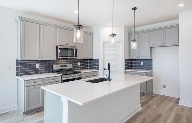 kitchen featuring light wood-style floors, gray cabinets, a sink, stainless steel appliances, and baseboards