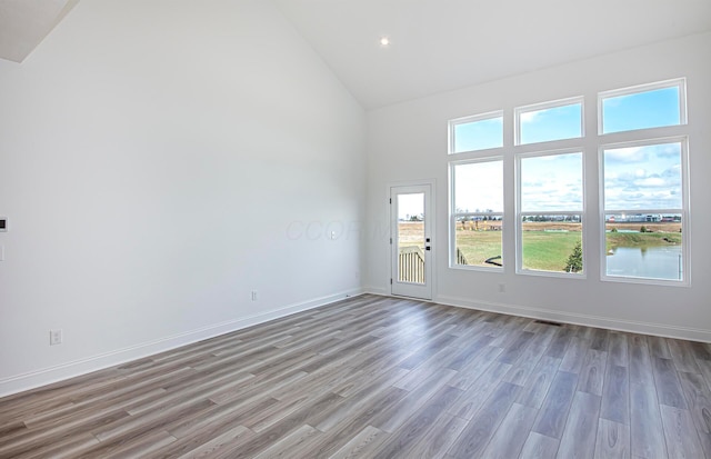 empty room featuring wood finished floors, high vaulted ceiling, baseboards, and visible vents