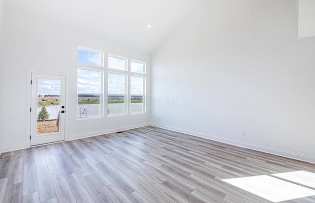empty room with high vaulted ceiling, visible vents, light wood-type flooring, and baseboards