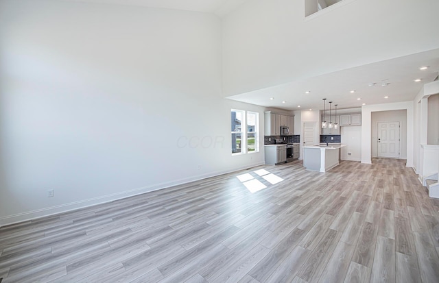 unfurnished living room with light wood-style flooring, recessed lighting, a towering ceiling, and baseboards