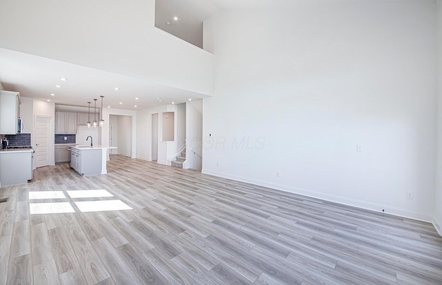 unfurnished living room featuring light wood-style flooring, recessed lighting, a sink, stairs, and baseboards