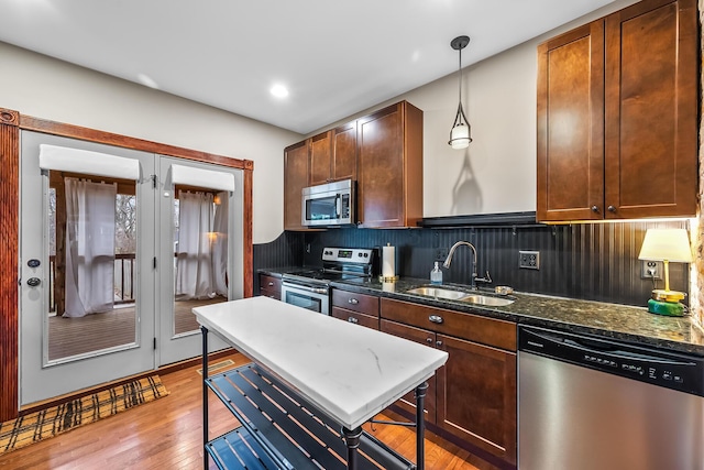 kitchen with sink, appliances with stainless steel finishes, tasteful backsplash, light hardwood / wood-style floors, and dark stone counters