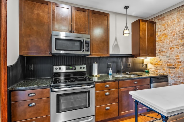 kitchen with sink, hanging light fixtures, stainless steel appliances, brick wall, and dark stone counters