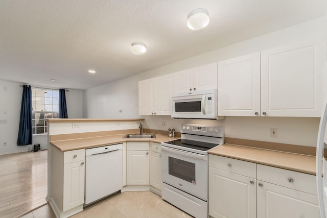 kitchen featuring white appliances, kitchen peninsula, sink, and white cabinets