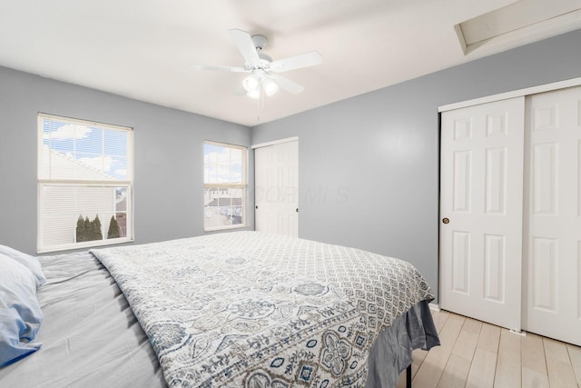 bedroom with ceiling fan, two closets, and light hardwood / wood-style floors