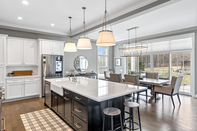 kitchen featuring white cabinets, a kitchen island with sink, pendant lighting, and light countertops