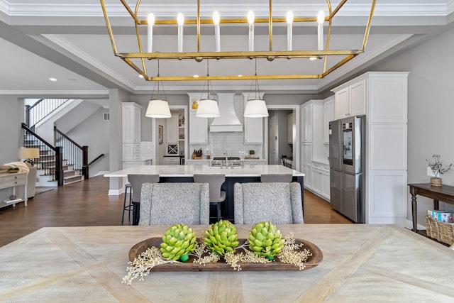 kitchen featuring premium range hood, light countertops, an island with sink, smart refrigerator, and decorative light fixtures