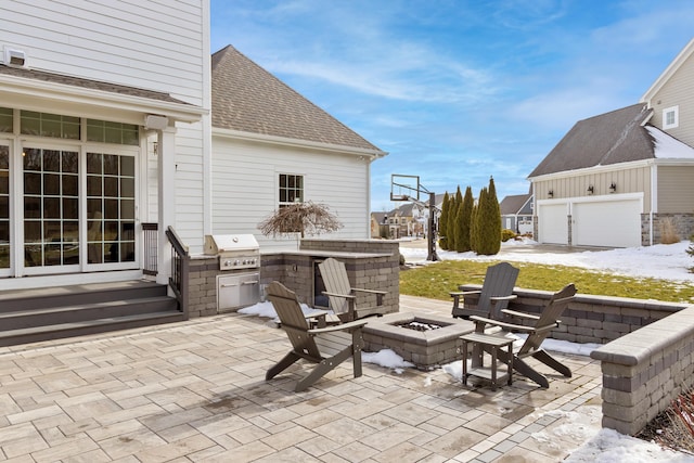 snow covered patio with an outdoor fire pit, area for grilling, an outdoor kitchen, and entry steps