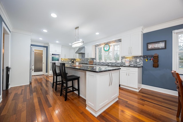 kitchen featuring white cabinets, stainless steel appliances, crown molding, and wall chimney range hood