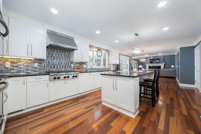 kitchen with stainless steel gas cooktop, open floor plan, white cabinets, and wall chimney range hood