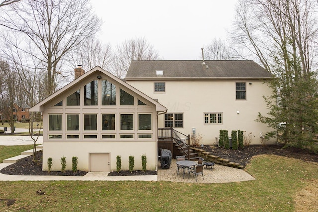 back of house with stucco siding, a lawn, a chimney, and a patio area