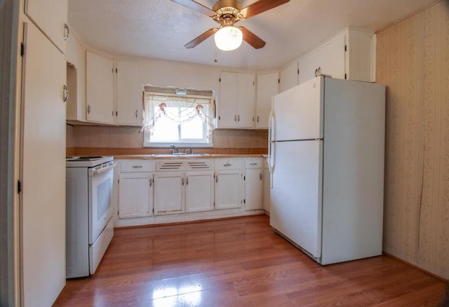 kitchen with a sink, white appliances, light wood-style flooring, and wallpapered walls