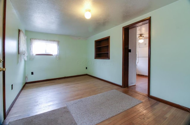 empty room with a textured ceiling, built in shelves, hardwood / wood-style flooring, and baseboards