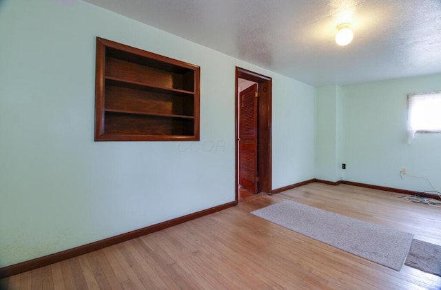 spare room featuring built in shelves, hardwood / wood-style floors, baseboards, and a textured ceiling