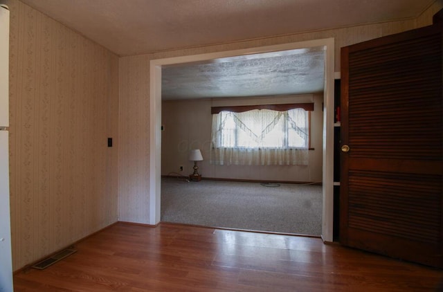 hall with baseboards, wood finished floors, visible vents, and wallpapered walls