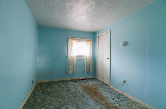 empty room featuring carpet floors, a textured ceiling, and baseboards