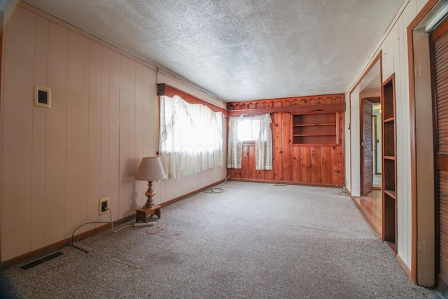 unfurnished room featuring carpet, visible vents, wooden walls, a textured ceiling, and baseboards