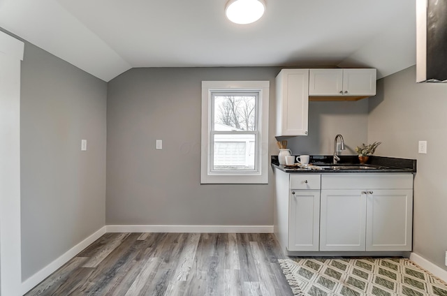 kitchen with hardwood / wood-style flooring, lofted ceiling, sink, and white cabinets