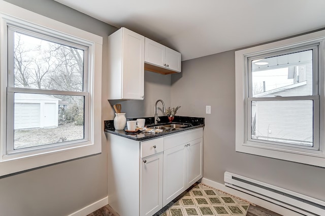 kitchen featuring white cabinetry, dark stone counters, sink, and a baseboard heating unit