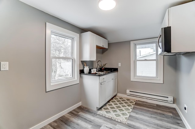 kitchen with baseboard heating, white cabinetry, sink, and light hardwood / wood-style floors