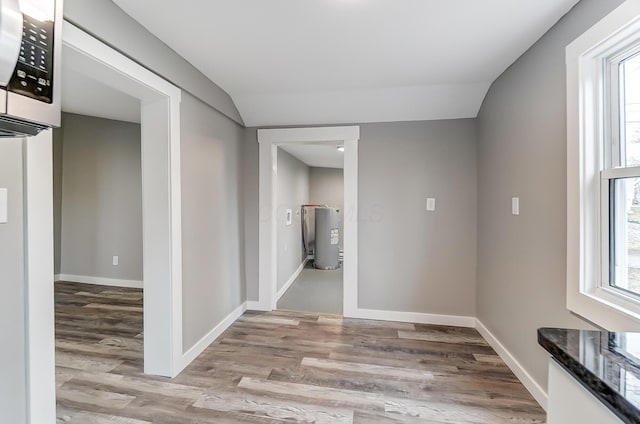 corridor with lofted ceiling, light hardwood / wood-style floors, electric water heater, and a wealth of natural light