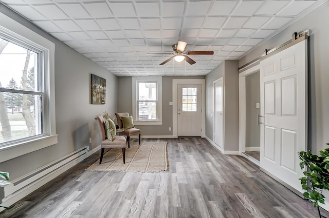 living area with a baseboard heating unit, wood-type flooring, a barn door, and ceiling fan