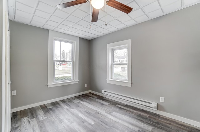 spare room with a baseboard radiator, plenty of natural light, wood-type flooring, and a drop ceiling