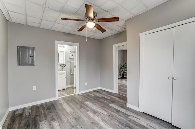 unfurnished bedroom with ensuite bath, a paneled ceiling, electric panel, a closet, and light wood-type flooring