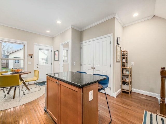 kitchen featuring crown molding, a center island, light hardwood / wood-style flooring, and dark stone countertops