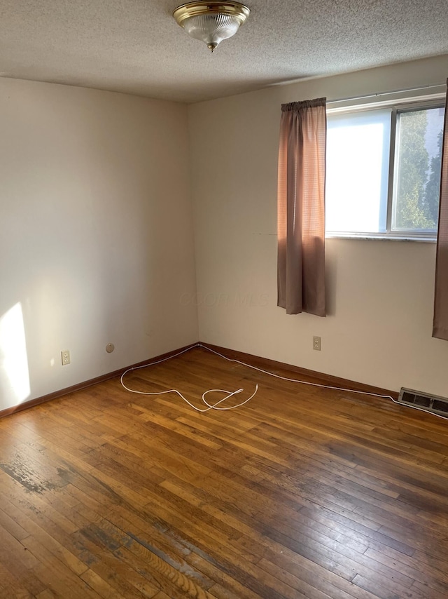 spare room featuring a textured ceiling and dark hardwood / wood-style flooring