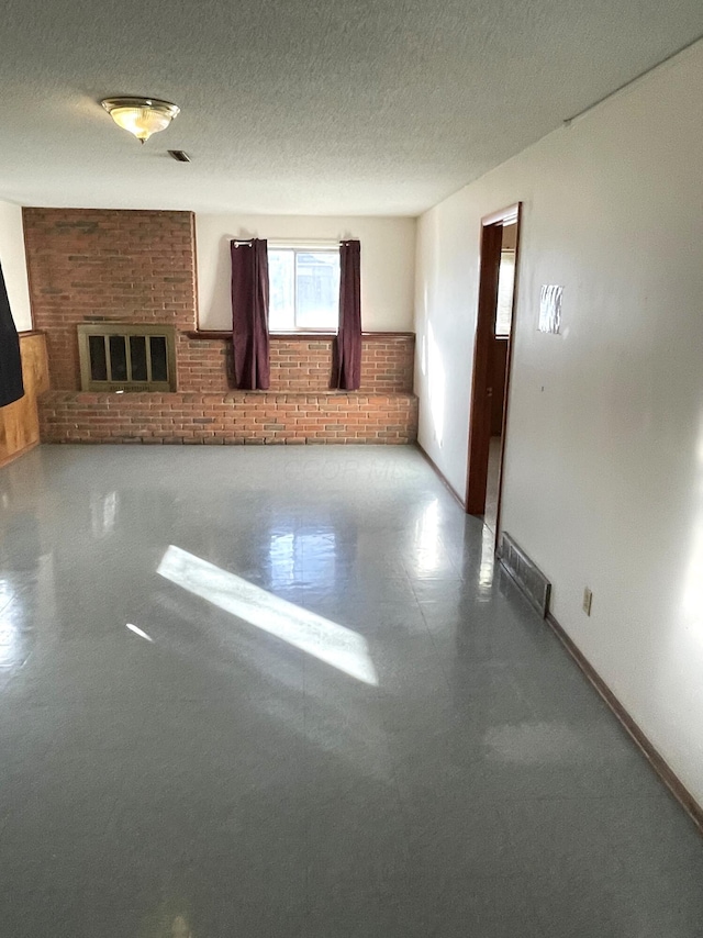 spare room featuring a fireplace, a textured ceiling, and brick wall