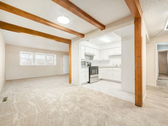 unfurnished living room with beamed ceiling, sink, and light carpet