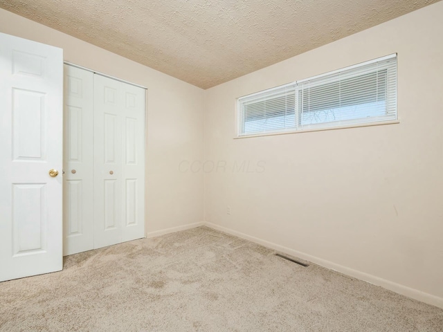 unfurnished bedroom featuring light colored carpet, a textured ceiling, and a closet