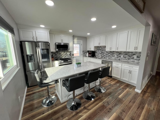 kitchen with white cabinets, a kitchen bar, a center island, light stone counters, and stainless steel appliances