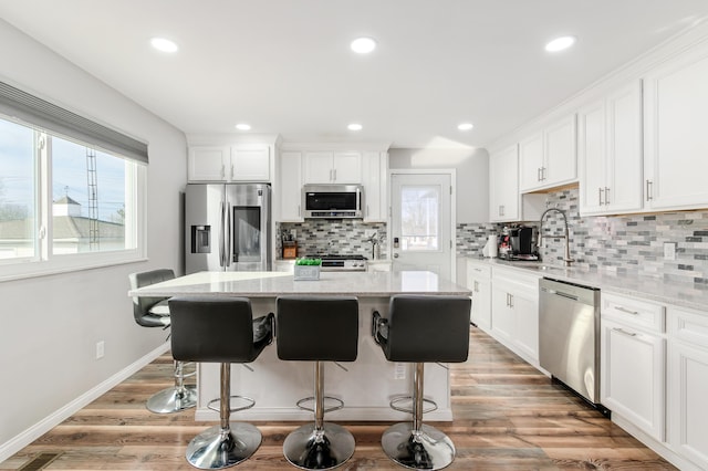 kitchen featuring a kitchen island, appliances with stainless steel finishes, sink, white cabinets, and light stone counters