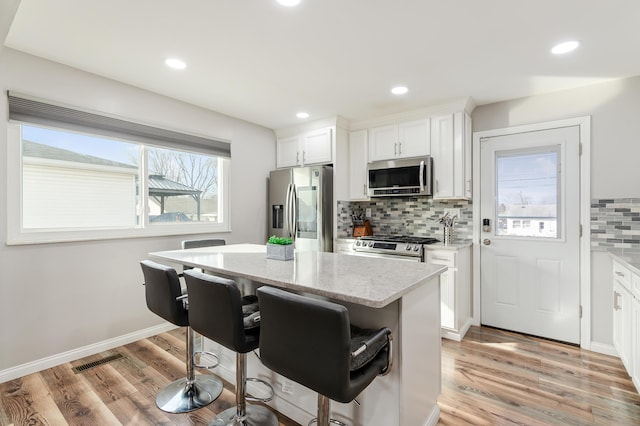 kitchen featuring light stone counters, stainless steel appliances, a center island, and white cabinets