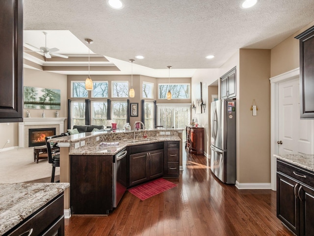 kitchen featuring dark brown cabinetry, sink, light stone counters, a tile fireplace, and stainless steel appliances