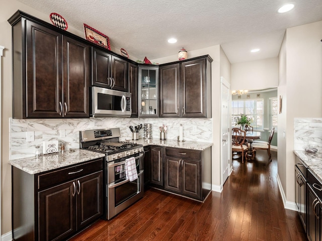 kitchen with stainless steel appliances, light stone countertops, dark brown cabinets, and backsplash