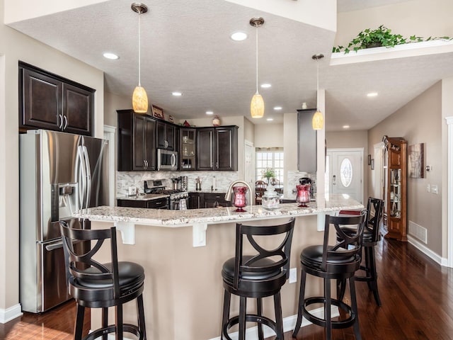 kitchen with dark brown cabinets, stainless steel appliances, a breakfast bar, and hanging light fixtures