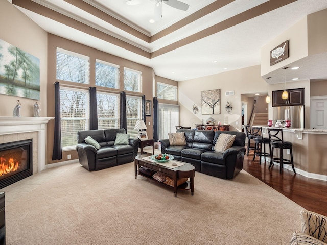 living room featuring a fireplace, a high ceiling, ceiling fan, a raised ceiling, and crown molding