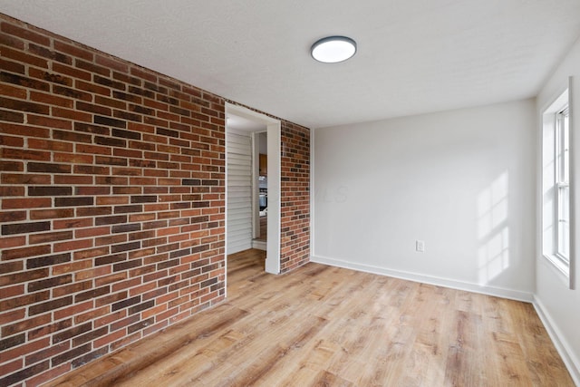 spare room featuring brick wall, plenty of natural light, light hardwood / wood-style floors, and a textured ceiling