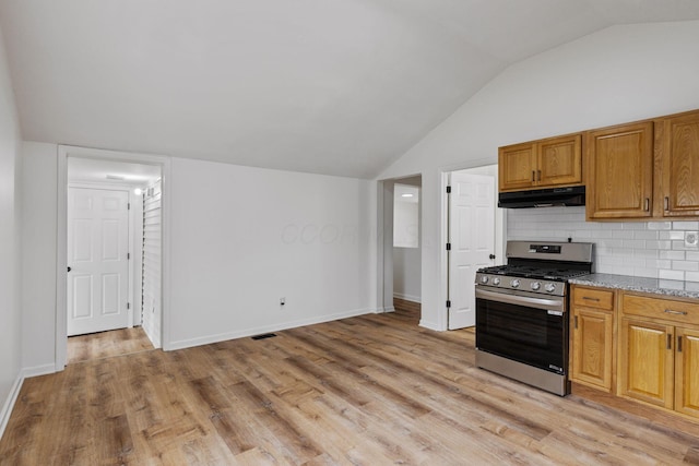 kitchen with lofted ceiling, light wood-type flooring, stainless steel range with gas cooktop, light stone countertops, and backsplash