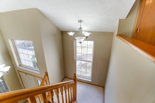 stairway with carpet flooring, a notable chandelier, and a textured ceiling