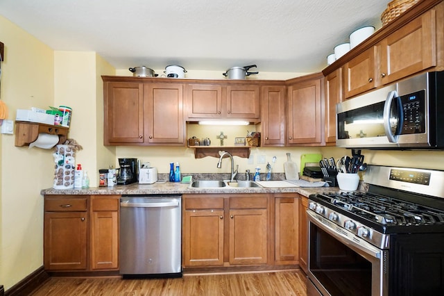 kitchen featuring light stone counters, sink, light hardwood / wood-style floors, and appliances with stainless steel finishes