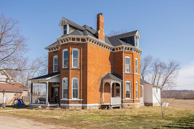 view of front facade with brick siding, an attached garage, a chimney, and a front lawn