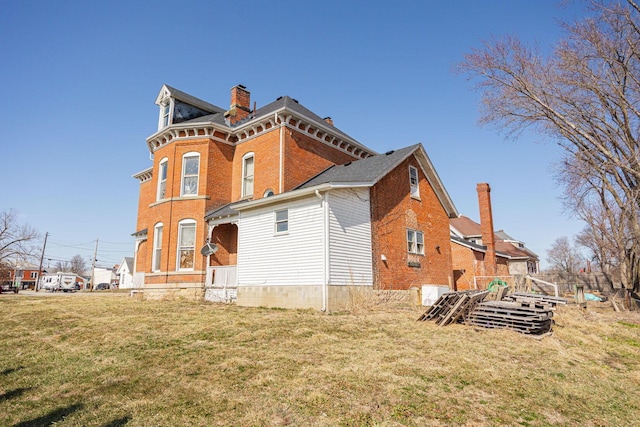 rear view of house featuring a yard, brick siding, and a chimney