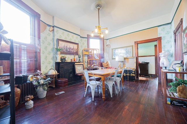 dining area featuring a chandelier, visible vents, hardwood / wood-style floors, radiator heating unit, and wallpapered walls